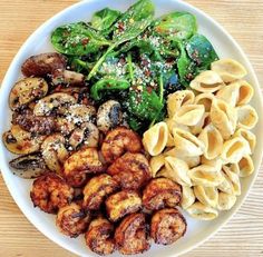 a white plate topped with pasta, spinach and other foods on top of a wooden table