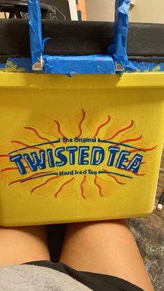 a yellow box with the words twisted tea painted on it's side sitting in someones lap