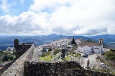 an old stone wall in the middle of a small town with mountains in the background