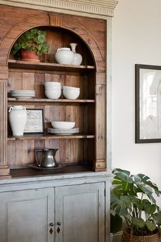 a wooden hutch with plates and bowls on it in a living room next to a potted plant