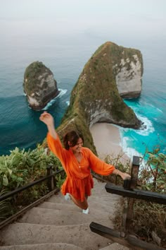 a woman in an orange dress is jumping down some stairs near the ocean and cliffs