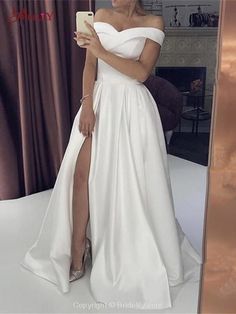 a woman standing in front of a mirror wearing a white dress with thigh high slit