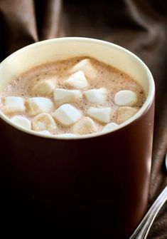 a cup of hot chocolate with marshmallows in it and a spoon next to it