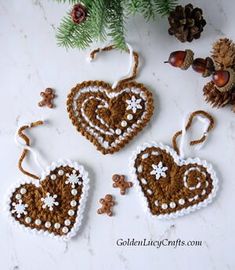 three crocheted heart ornaments on a table with pine cones and evergreen branches in the background