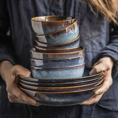 a woman holding a stack of blue and brown dishes in her hands while wearing a black shirt