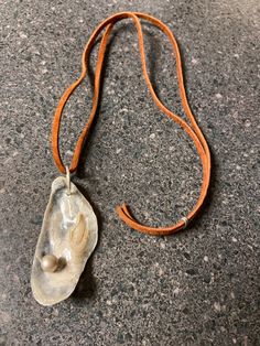 a necklace with a shell on it sitting on top of a stone floor next to a brown cord