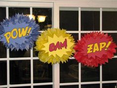 three different colored paper decorations hanging from the side of a window with words pow and zap on them