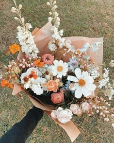 a person holding a bouquet of flowers in their hand on the ground with grass and dirt behind them