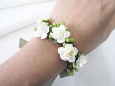 a woman's arm wearing a bracelet with white flowers and green leaves on it