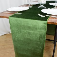 a green table runner on top of a wooden table with white plates and silverware