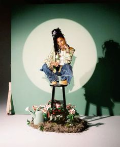 a woman sitting on top of a stool in front of a green wall holding a cell phone