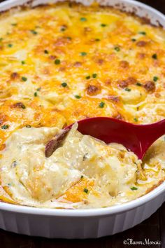 a casserole dish filled with cheese and meat being spooned into it by a red spatula