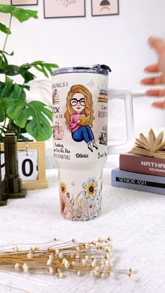 a white coffee cup with a drawing of a woman on it and some flowers in the background