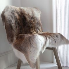 a chair with fur on it in front of a white wall and window sill