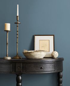 a wooden table topped with a bowl and two candles next to a framed photograph on the wall