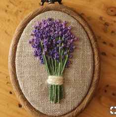 a close up of a embroidery on a wooden surface with purple flowers in the middle