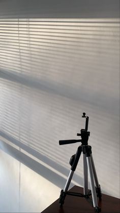 a tripod sitting on top of a wooden table next to a window covered in blinds