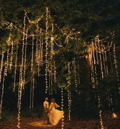 a bride and groom walking through the woods at night with fairy lights strung all around them