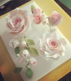 three pink roses sitting on top of a white cake with green leaves and flowers in the middle