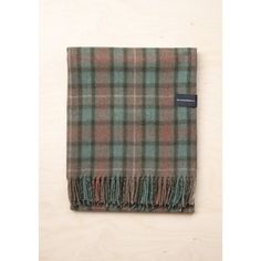 the green and blue plaid blanket is folded on top of a wooden surface with a tag