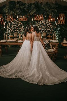 two women in wedding dresses standing next to each other with candles on the wall behind them