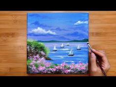 someone is painting boats in the water on a wooden table with pink flowers and green trees