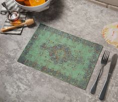 a place mat, utensils and oranges are on the floor next to a bowl of oranges