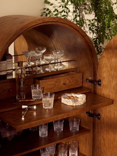 a wooden cabinet filled with glasses next to a potted plant