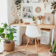 a desk with plants and pictures on the wall in a room that has white walls