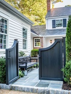 an open gate leading to a house with a bench in the foreground and bushes on either side