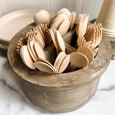 wooden utensils are arranged in a bowl on a marble countertop next to plates and cups