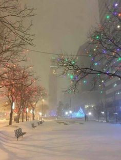 a city street covered in snow with christmas lights on trees and people walking down the sidewalk