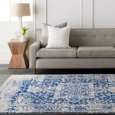 a living room with a gray couch and blue rug on the floor next to a lamp