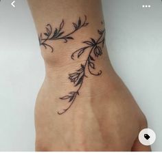 a woman's hand with a tattoo on the wrist that has flowers and leaves drawn on it