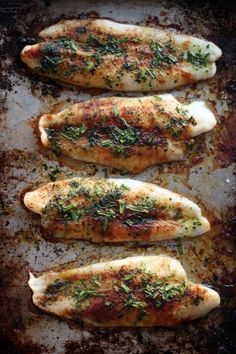 three fish fillets with herbs and seasonings on a baking sheet, ready to go into the oven