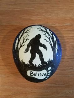 a painted rock that says believe with a bigfoot walking through the woods on it