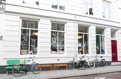 several bicycles are parked in front of a white building with many windows and benches on the sidewalk