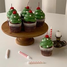 cupcakes decorated with green frosting and red cherries on a cake stand