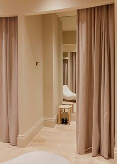 a bedroom with beige curtains and a white chair in the corner next to a window