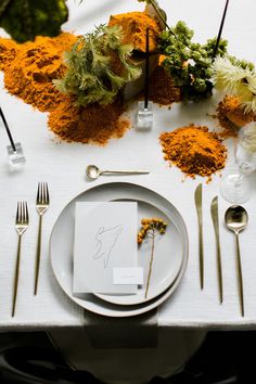 the table is set with white plates, silverware and orange sprinkles