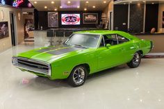 a green muscle car in a showroom with neon signs on the wall behind it