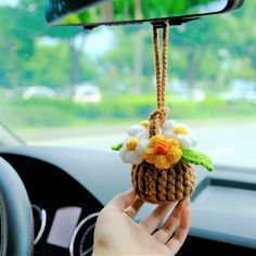 a hand holding a small basket with flowers hanging from it's side in a car