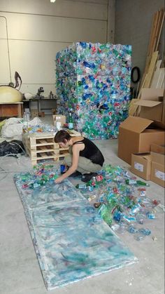 a man kneeling down on top of a pile of plastic bottles in a room filled with boxes and other items