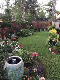 a garden with lots of flowers and plants in the grass next to a wooden fence