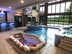 a large indoor swimming pool with seating area and television on the wall, in front of an open floor plan