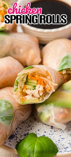 chicken spring rolls on a plate with dipping sauce and green leaves around the wrapper