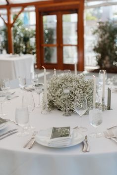 the table is set with silverware and white linens, candles, and baby's breath flowers