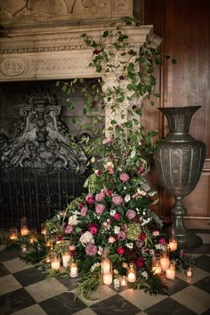 flowers and candles are arranged on the floor in front of a fireplace with an ornate urn