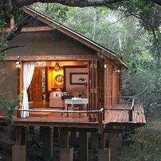 a small cabin in the middle of some trees with curtains on it's windows