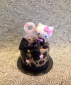 two hello kitty figurines sitting on top of a black and white decorated cake